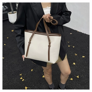 Close-up of white lychee leather tote bag with brown straps in an autumn street setting