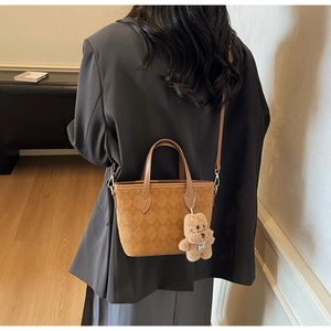 Brown quilted crossbody bucket bag with plush bear charm worn by a model in black blazer