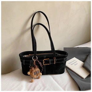 Detail of black suede tote bag with decorative buckle strap and plush charm