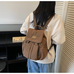 Brown canvas backpack with embroidered detail shown on model in a retro setting