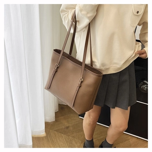Close-up of brown litchi grain leather tote bag featuring gold adjustable strap buckles