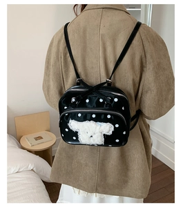 Detailed view of black polka dot backpack with plush animal accent and silver zippers