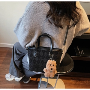 Detail of black quilted bucket bag featuring a brown teddy bear charm and adjustable strap