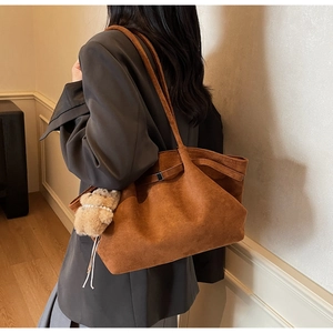 Braune Wildleder-Tragetasche mit Teddybär-Anhänger, getragen von einem Modell