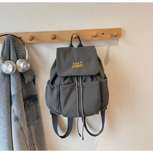 Detail of grey canvas backpack featuring yellow embroidery and drawstring closure