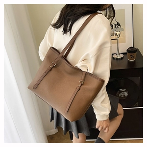 Detailed back view of large brown lychee grain tote bag worn by a model in a minimal setting
