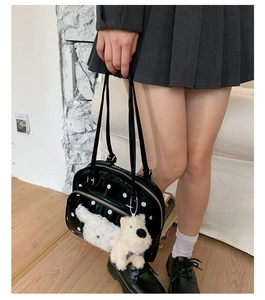 Detail of black patent leather tote with white polka dots and plush dog charm