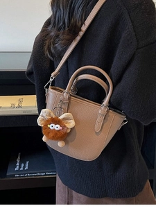 Fashionable light brown leather bucket bag with a cute plush monster charm and strap