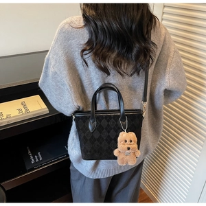 Detail of black quilted crossbody bag with CF embossing and a plush bear charm on a model