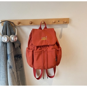 Detail of a brick-red canvas backpack with drawstring closure and yellow embroidery logo