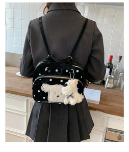 Detail of glossy black polka dot backpack with a cute plush dog pendant charm