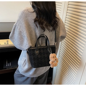 Detail of a black quilted tote bag with a plush bear charm worn in a lifestyle library setting
