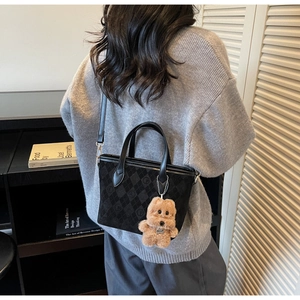 Detail of black suede bucket bag with quilted patterns and a cute brown bear charm