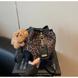 Detail of leopard print bucket bag with gold buckle and brown plush bear charm accessory