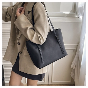 Detailed view of black litchi pattern leather tote bag with gold metal buckle accents