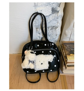 Detail of black polka dot handbag with plush puppy charm and glossy finish texture