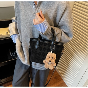 Detail of black checkered suede tote bag featuring a cute plush bear charm accessory