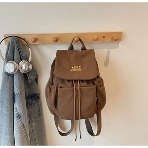 Detail of dark brown canvas backpack featuring yellow embroidery and drawstring closure