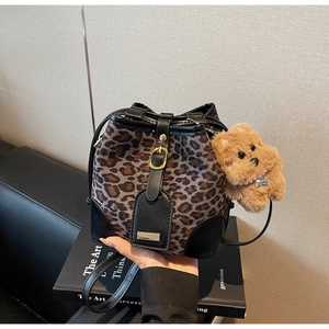 Detail of leopard print bucket bag featuring black leather trim and plush puppy charm