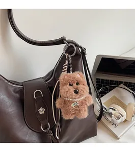 Close-up of a brown plush puppy charm with a pearl necklace on a leather handbag