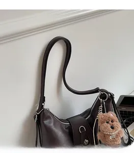 Close-up of brown faux leather shoulder bag with adjustable strap and cute bear charm