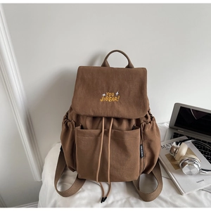 Detailed view of brown canvas backpack with yellow embroidery and side brand label