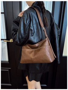 Detail of dark brown leather tote bag with logo on a model in black leather jacket