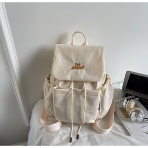 Detail of off-white canvas backpack featuring drawstring closure and top flap embroidery