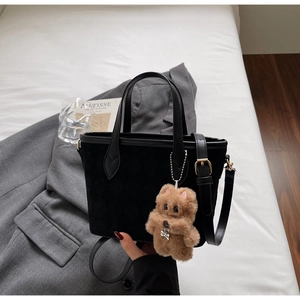 Close-up of black suede bucket bag with leather trim and plush bear keychain detail