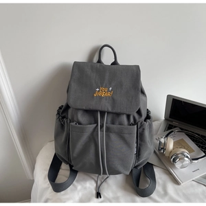 Close-up of minimalist grey backpack with yellow embroidery and side pocket detail