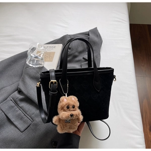 Detail of black suede bucket bag with geometric texture and plush dog pendant charm