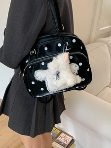 Retro black polka dot messenger bag with plush puppy charm worn by a model in a room