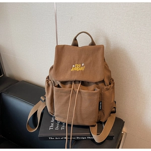 Detail view of coffee brown canvas backpack with flap cover and yellow embroidery text