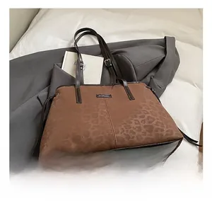 Brown leopard print tote bag with dark leather handles on a grey suit and white bedding