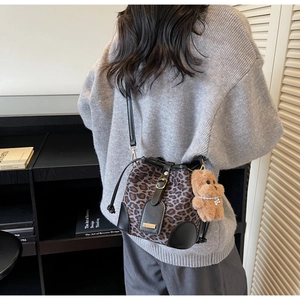 Detail view of leopard print bucket bag with drawstring and plush dog charm on a model