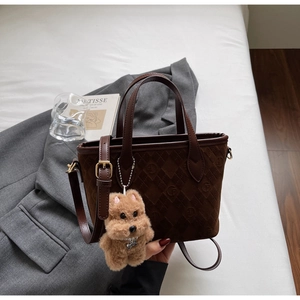 Detail of dark brown quilted suede tote bag with plush dog charm and long shoulder strap