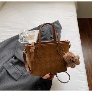 Detail of a brown suede bucket bag with embossed patterns and a cute teddy bear charm
