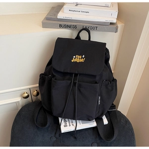 Detail of black backpack with yellow embroidery, drawstring closure, and side woven label