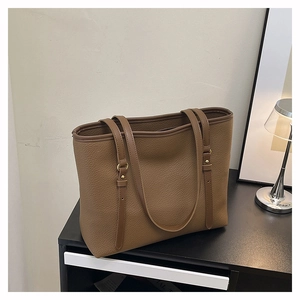 Detailed close-up of brown pebbled leather texture and metal rivets on the tote shoulder bag