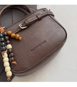 Close-up of brown leather handbag with embossed fashion logo and beaded wooden charm