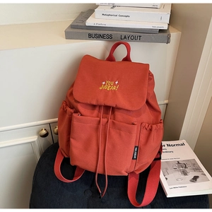 Close-up of orange canvas backpack featuring yellow embroidery and side pocket detail