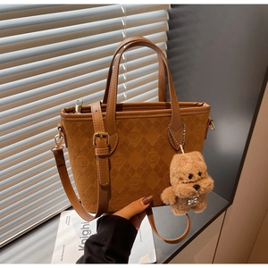 Detail of brown embossed bucket bag with plush charm and adjustable shoulder strap