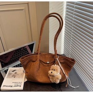 Close-up of brown suede tote bag with metal buckle and cute bear charm in warm sunlight