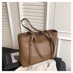 Detailed shot of large brown lychee leather tote bag with slim straps on a book