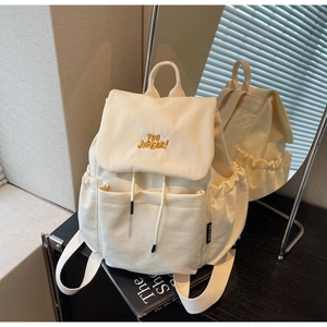 Detail of cream nylon backpack featuring yellow embroidery and drawstring closure