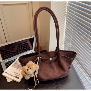 Detail of dark brown suede tote bag with plush dog charm and metal buckle accent