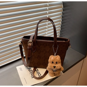 Close-up of brown suede tote bag with diamond pattern and cute plush dog charm on window sill