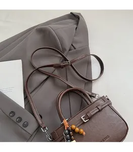 Detail of a dark brown leather handbag with wooden bead charm and adjustable strap
