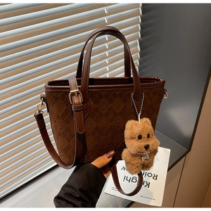 Detail of brown suede tote bag with diamond quilting and plush puppy charm accessory