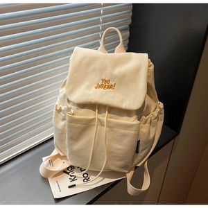 Detail of beige canvas backpack featuring yellow brand embroidery and drawstring closure